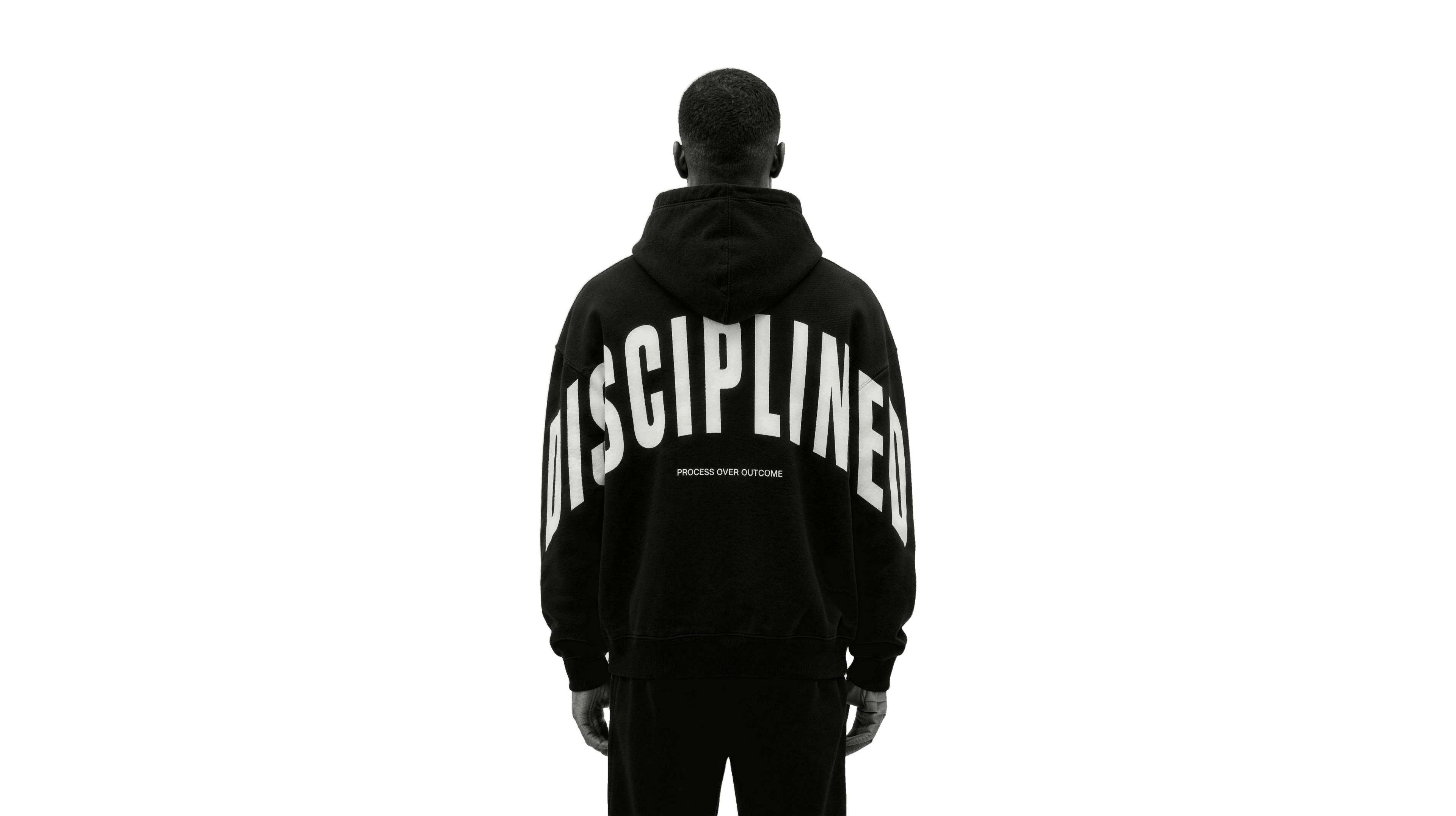 Back view of the DISCIPLINED heavyweight hoodie: an arched DISCIPLINED wordmark over PROCESS OVER OUTCOME, worn by a figure standing back to camera.