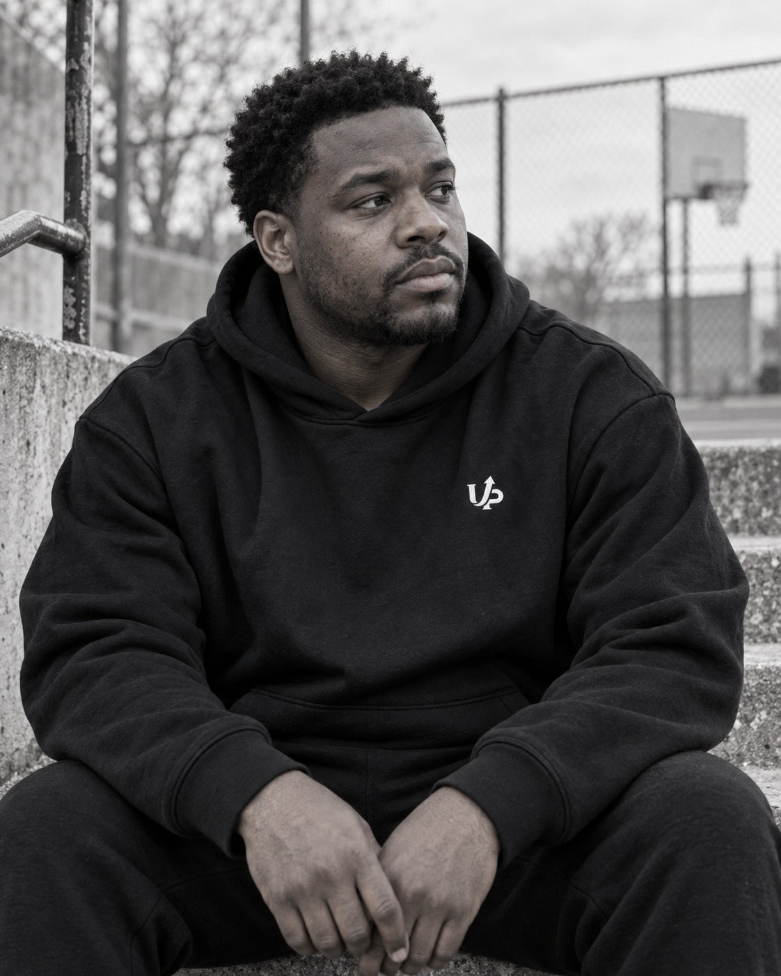 Generated monochrome campaign portrait of a man resting beside a court in the DISCIPLINED hoodie, with the small chest monogram visible